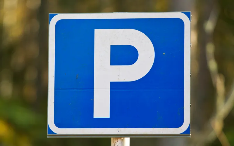 En blå och vit parkeringsskylt med träd i bakgrunden.