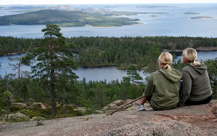 Bild på två kvinnor som sitter på Skuleberget i Skulebergets naturreservat och tittar ut över utsikten mot havet.
