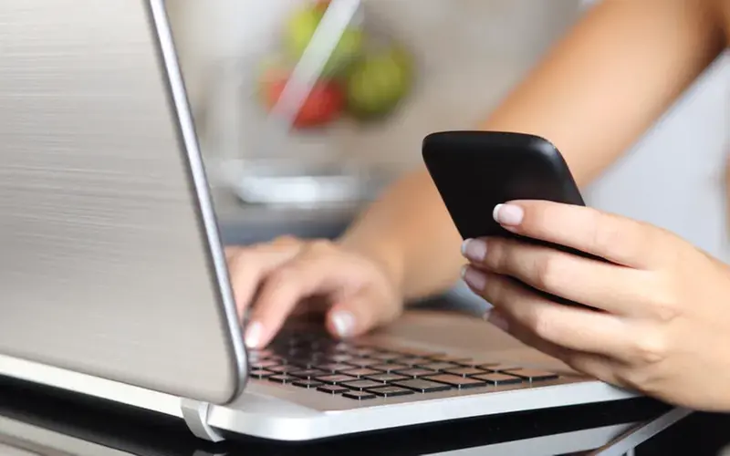 Person som använder datorn och mobiltelefon
